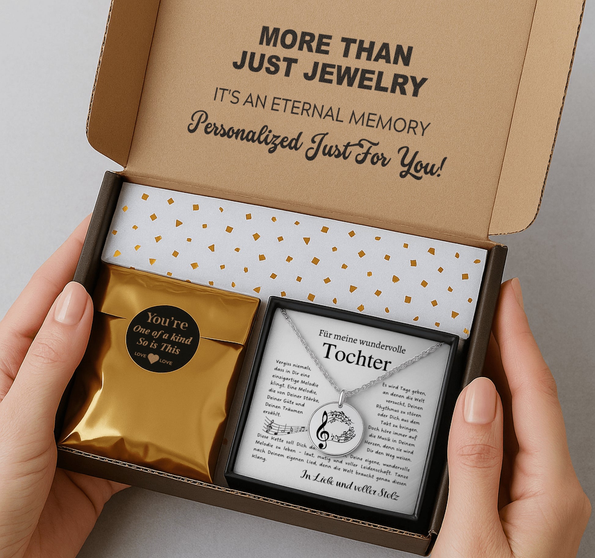 Eine goldene Halskette mit einem runden Anhänger, der mit einem Notenschlüssel und Musiknoten graviert ist. Die Kette wird in einer edlen, schwarzen Geschenkbox auf einer Karte mit einem inspirierenden, emotionalen Spruch präsentiert. Die liebevolle Aufmachung mit zarten Blütenblättern im Hintergrund positioniert den Schmuck als hochwertiges und bedeutungsvolles Geschenk für einen besonderen Menschen.