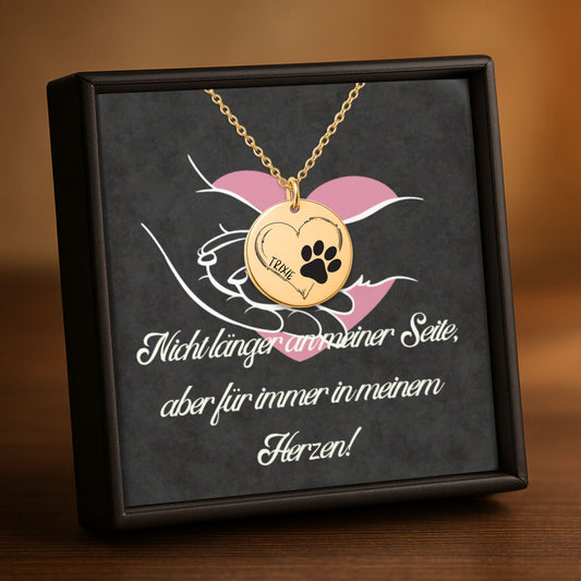 Personalisierte Hundepfoten-Halskette mit rundem Anhänger aus Edelstahl in 18K Goldoptik, Rosé-Gold plattiert oder in Edelstahl Silber. Der Anhänger zeigt eine schwarze Hundepfote, ein Herz und den Namen des Hundes. Die Rückseite kann mit einer persönlichen Lasergravur versehen werden. Die Kette ist 45 cm lang und besitzt eine 5 cm Verlängerung. Ein emotionaler Hund Gedenkschmuck und besonderes Geschenk für Hundebesitzer und Hundeliebhaber zur Erinnerung an einen geliebten Vierbeiner.