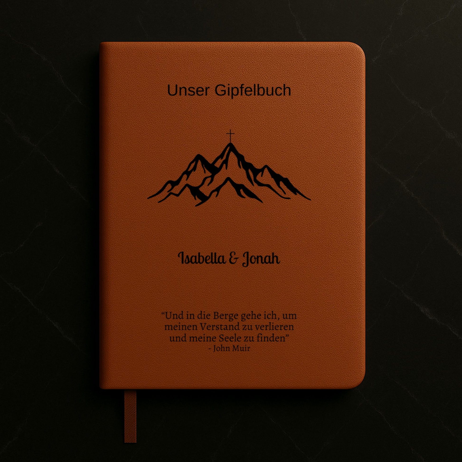 Ein personalisiertes Gipfelbuch in A5 mit einem braunen, veganen Ledereinband liegt auf einer hellen Oberfläche. Auf dem Cover sind in Schwarz ein Bergmotiv mit einem Gipfelkreuz und der Schriftzug "Unser Gipfelbuch" zu sehen. Darunter stehen die personalisierten Namen "Isabella & Jonah" sowie ein inspirierendes Zitat von John Muir über die Berge.
