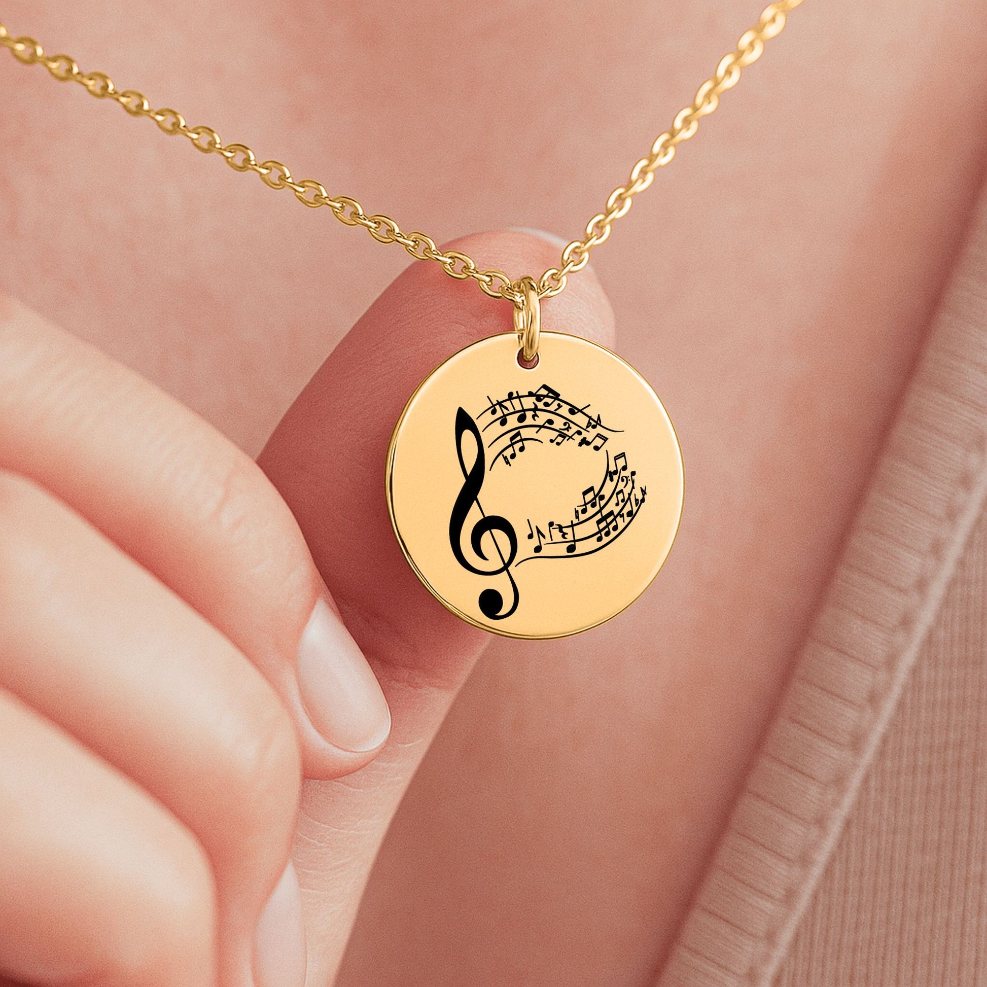 Eine goldene Halskette mit einem runden Anhänger, der mit einem Notenschlüssel und Musiknoten graviert ist. Die Kette wird in einer edlen, schwarzen Geschenkbox auf einer Karte mit einem inspirierenden, emotionalen Spruch präsentiert. Die liebevolle Aufmachung mit zarten Blütenblättern im Hintergrund positioniert den Schmuck als hochwertiges und bedeutungsvolles Geschenk für einen besonderen Menschen.