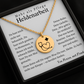Goldene Halskette mit runden Anhänger, auf dem ein Stethoskop ein Herz bildet und ein kleines Plus-Zeichen daneben steht. Die Kette liegt in einer schwarzen Schmuckbox mit einer Dankeskarte. Auf der Karte steht: 'Mehr als Pflege – Heldenarbeit'. Umgeben von rosa Rosenblättern."